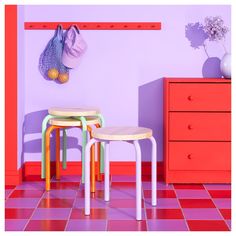 two small stools in front of a purple wall and red dresser with orange drawers