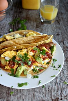 two breakfast tacos on a plate with eggs and avocado in the background