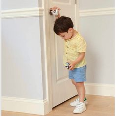 a little boy standing in front of a white door with his hand on the handle