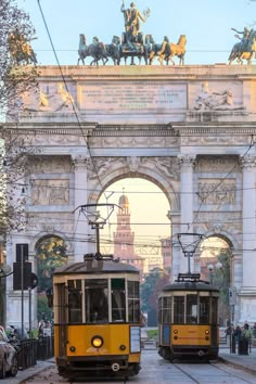 two yellow trolleys passing each other in front of an arch