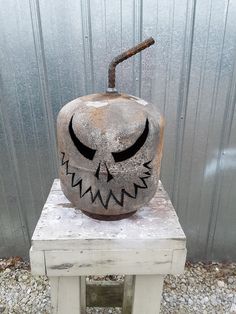 a cement pumpkin sitting on top of a wooden table next to a metal wall with an evil face painted on it