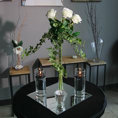 a vase filled with white roses sitting on top of a table next to two candles