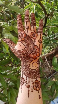 a hand with henna designs on it and some leaves in the back ground behind it