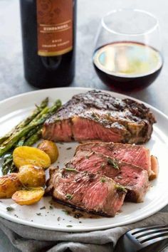 steak, asparagus and potatoes on a plate next to a bottle of wine