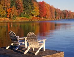 two chairs sitting on a dock in front of a body of water surrounded by trees