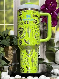 a green travel mug sitting on top of a table next to some white rocks and flowers