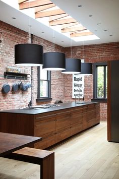 an open kitchen with brick walls and wooden flooring, along with black pendant lights hanging from the ceiling