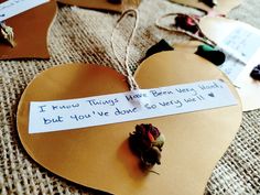 a heart shaped paper with a note attached to it and some flowers on the ground