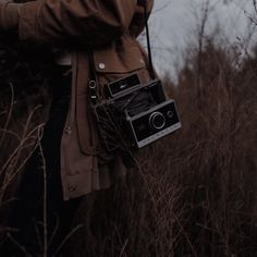 an old fashioned camera is held by someone's hand in a field with tall grass