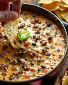 a hand dipping a tortilla chip into a bowl of chili cheese and black bean dip