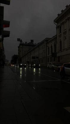 an empty city street at night with cars parked on the side walk and traffic lights