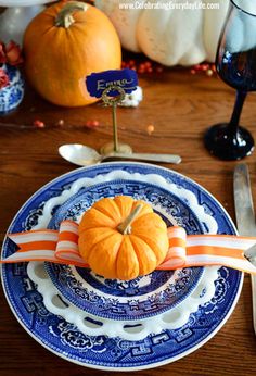 a blue and white plate with an orange pumpkin on it next to wine glasses, forks and knives