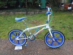 a blue and white bicycle parked on the side of a road next to a fence