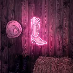 a neon cowboy boot sits next to a hay bale and a hat on the wall