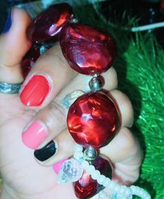 a woman's hand with red and pink nail polishes on her nails, next to green grass