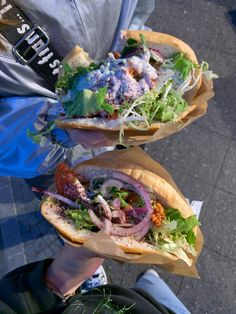 two sandwiches with lettuce, tomato and other toppings are held in their hands