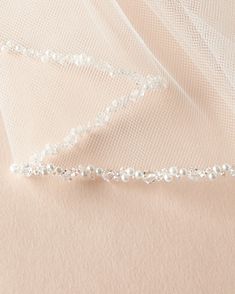 wedding veil with beaded edge laying on top of the fabric, close up view