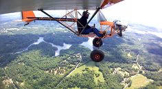 a man is sitting on the wing of an airplane flying over some trees and water