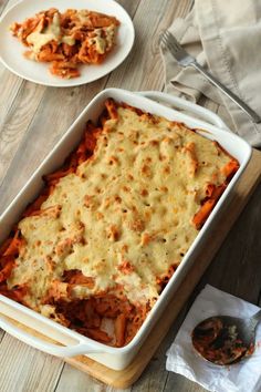 a casserole dish on a wooden table with two plates of food in the background