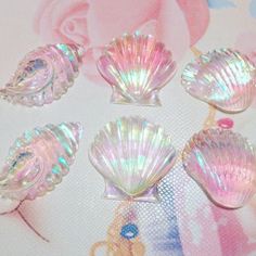 five glass seashells sitting on top of a pink tablecloth with roses in the background