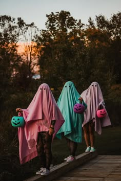 three girls dressed up in halloween costumes standing on a wooden bridge with pumpkins and ghost heads