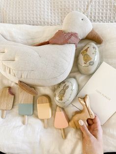 a person holding a wooden toy next to other toys on a white bed with an open book