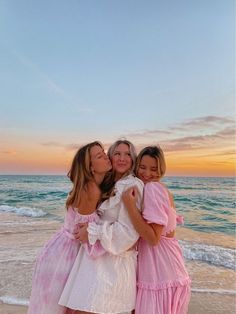 three girls in dresses hugging on the beach