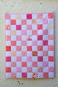 a pink and white patchwork quilt hanging on a wall