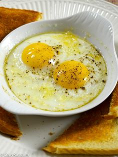 two fried eggs in a white bowl on top of toasted bread with seasoning