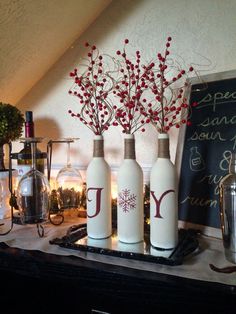 three white vases with red berries in them on a table next to a chalkboard