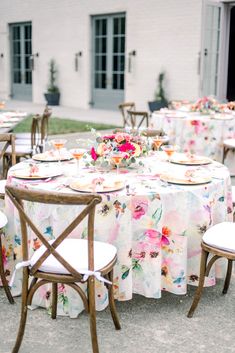 a table set up with flowers and plates for an outdoor wedding reception in front of a white brick building