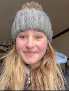 a woman with long blonde hair wearing a gray knitted hat and smiling at the camera