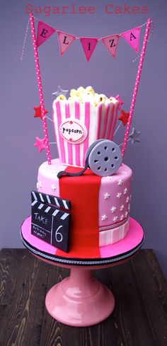 a pink and red birthday cake with popcorn, film claps and stars on it