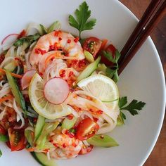 a white bowl filled with shrimp and veggies next to chopsticks on top of a wooden table