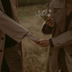 two people are holding hands and walking through the grass with flowers in their hands,