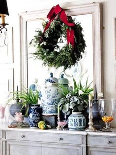 a christmas wreath is hanging on the wall above a dresser with vases and other decorations