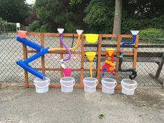 several buckets are lined up against a fence with plastic cups in front of them