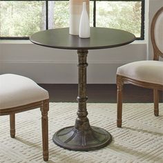 a round table with two chairs and a vase on the top, in front of a window