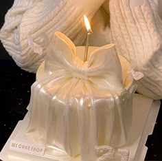 a white cake with a candle in it on a table next to some sweaters