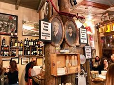 people are sitting at tables in a restaurant with pictures on the wall and wine bottles hanging from the ceiling