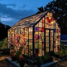 a glass house is lit up in the evening with flowers on it's side