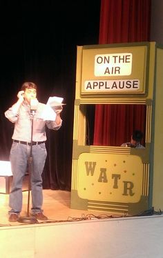 a man standing in front of a sign reading on the air applause with his hands to his face