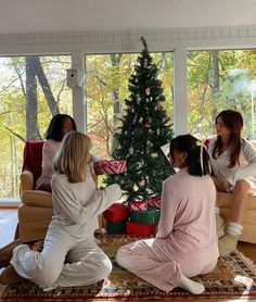 three women sitting on the floor in front of a christmas tree with presents under them