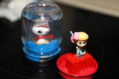 a small figurine is next to a toy in a glass jar on a table