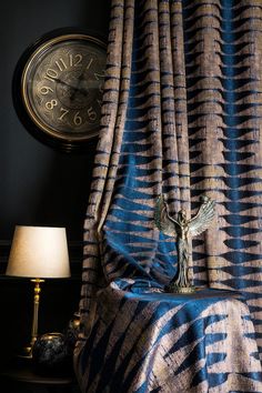 a clock on the wall next to a blue and gold curtain with an angel statue