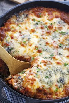 a casserole dish with cheese and spinach being stirred with a wooden spoon