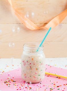 a jar filled with sprinkles next to a pink napkin and streamer