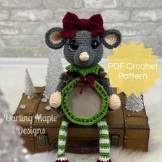 a crocheted mouse sitting on top of a suitcase with a red bow around its neck