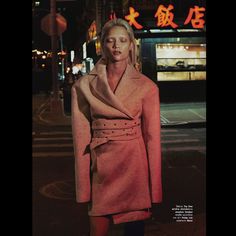 a woman is standing on the street at night wearing a coat and skirt with an attached belt