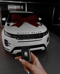 a person holding a cell phone in front of a white car with a red bow on it